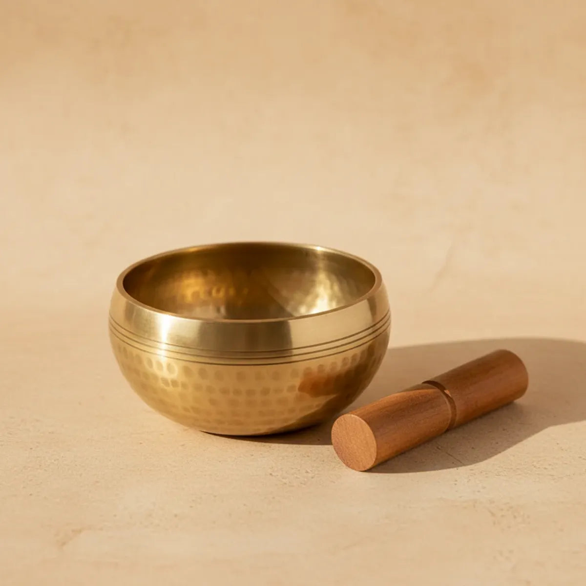 Bol chantant tibétain en laiton avec maillet en bois sur fond beige
