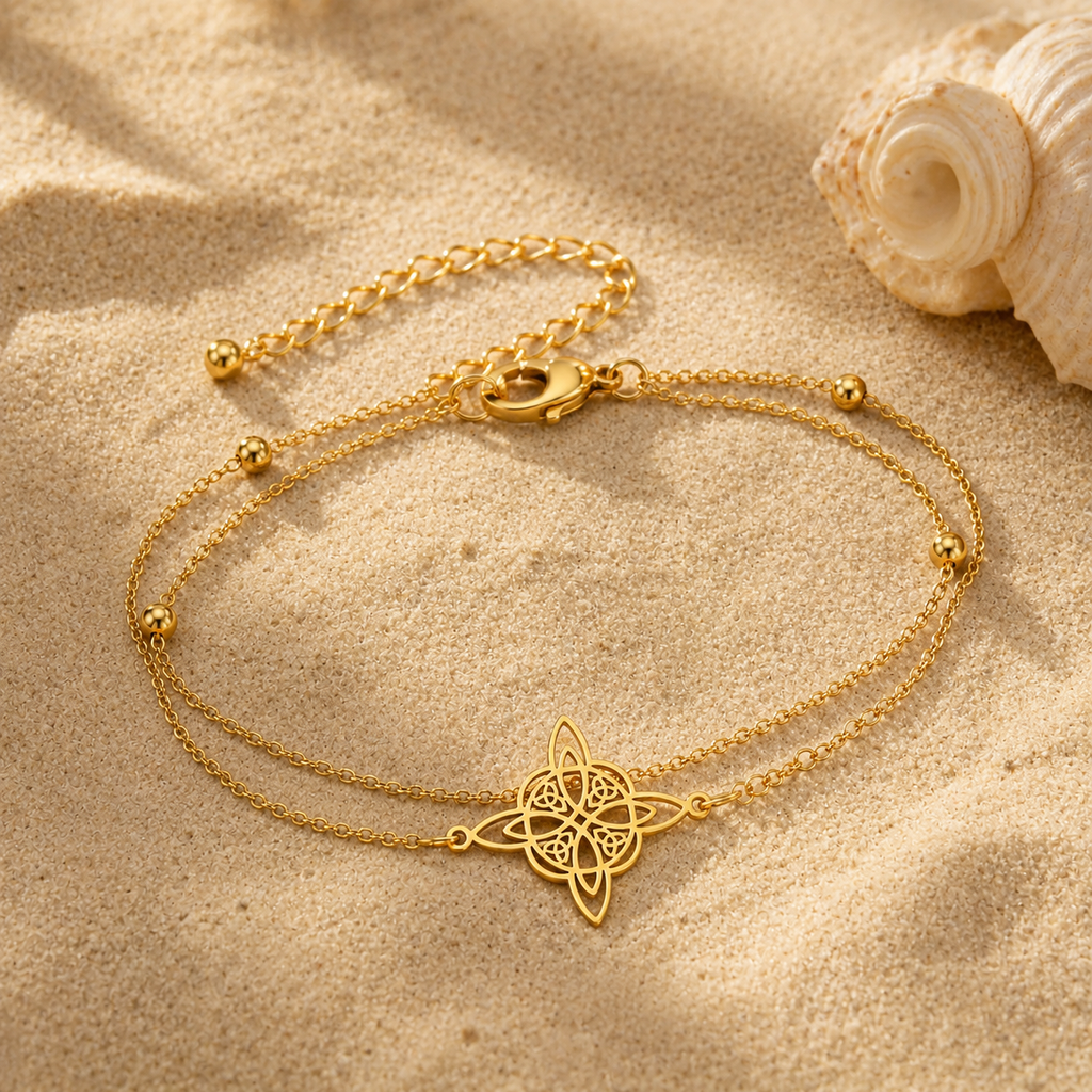 Chaîne de cheville double nœud de sorcière dorée sur le sable avec coquillage