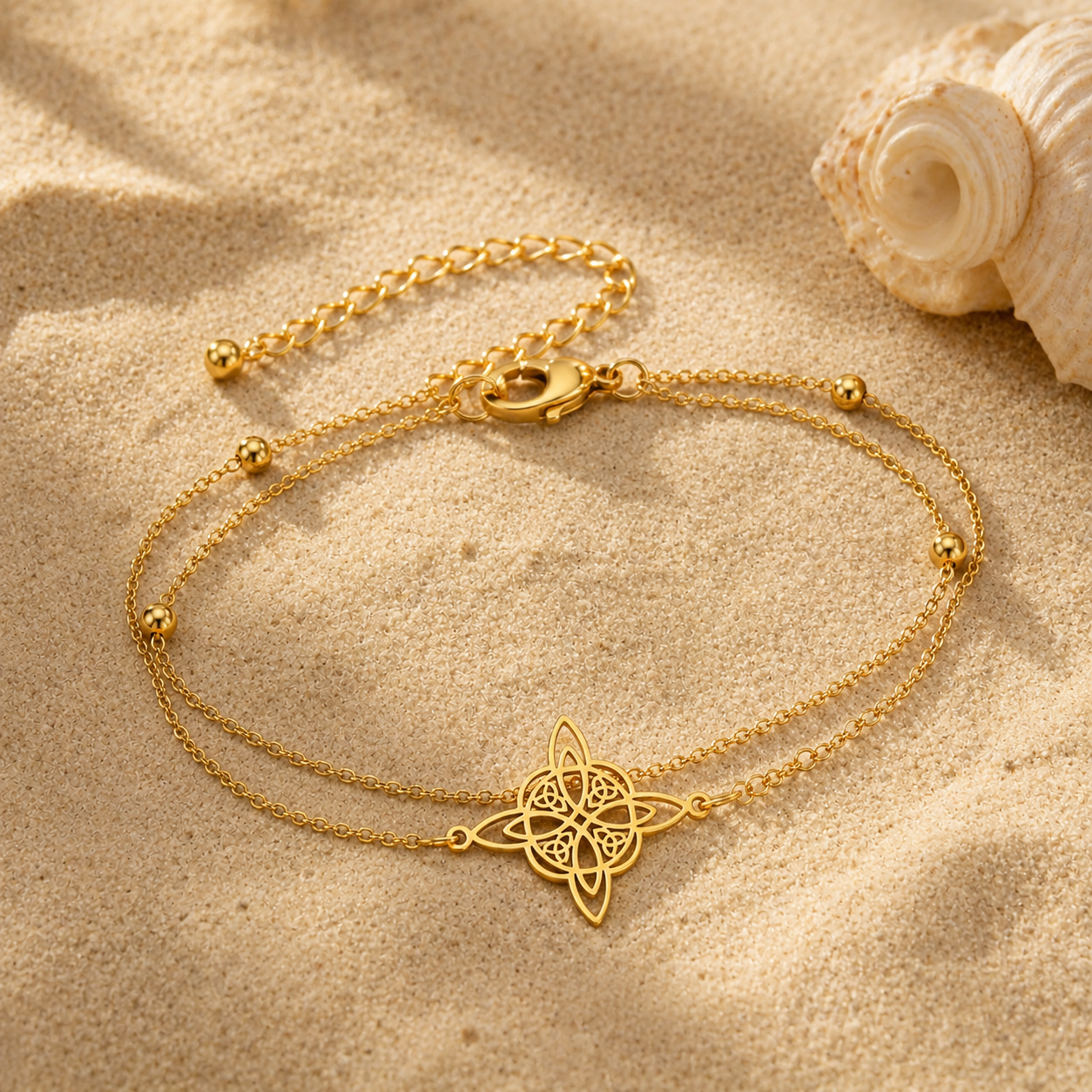 Chaîne de cheville double nœud de sorcière dorée sur le sable avec coquillage