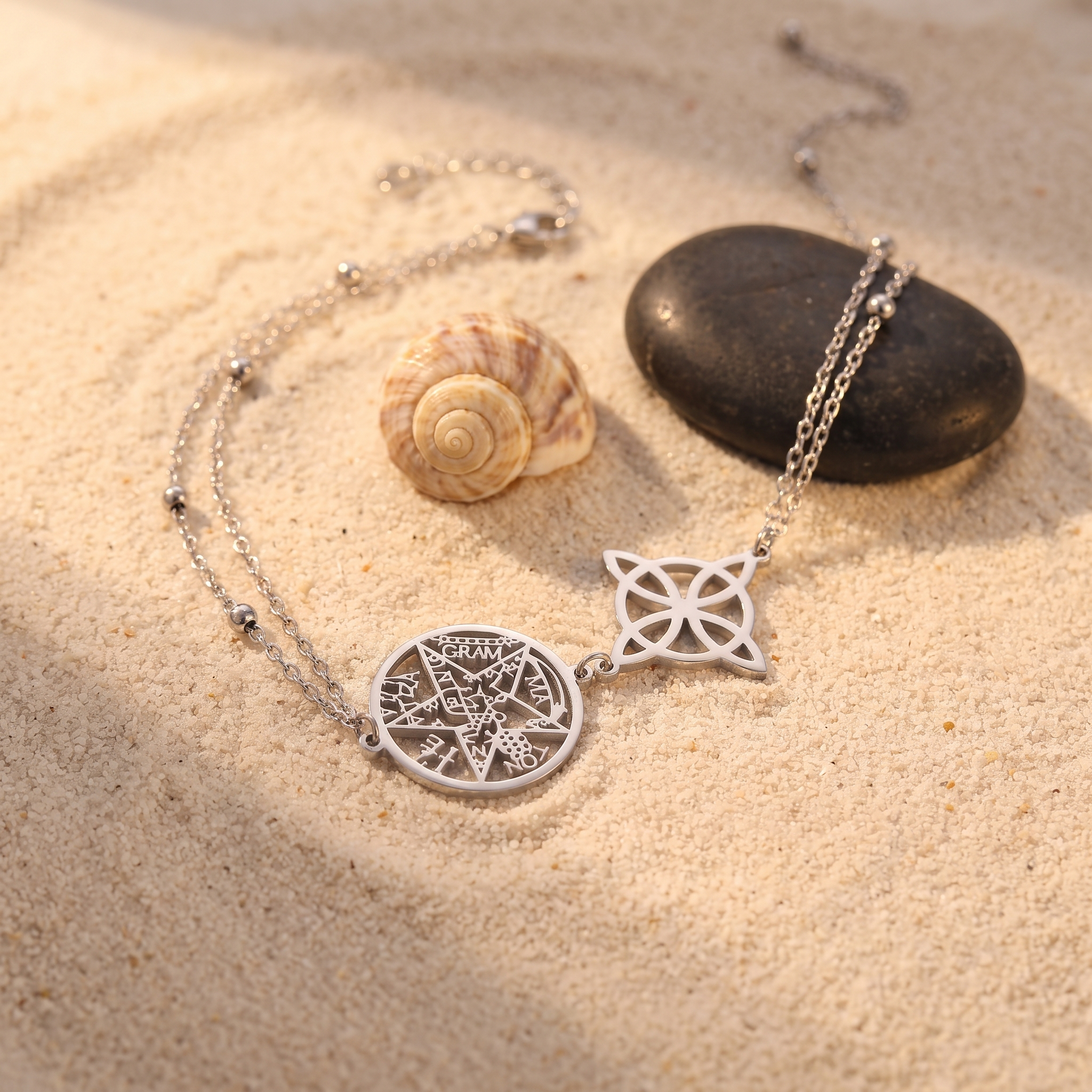 Chaîne de cheville nœud de sorcière et pentacle argentée sur le sable avec coquillage